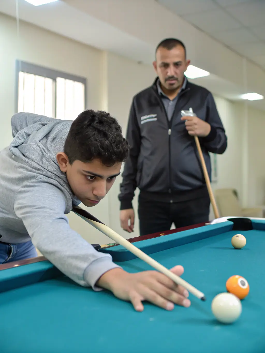 A senior member mentoring a newer player at BCB BILLARD CLUB BAIGNOIS, illustrating the club's intergenerational knowledge transfer and supportive community spirit.